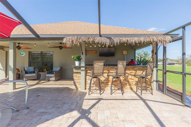 view of patio with ceiling fan, glass enclosure, and an outdoor bar