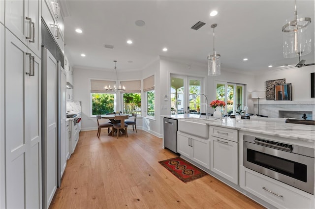 kitchen featuring visible vents, a sink, light wood-type flooring, appliances with stainless steel finishes, and crown molding