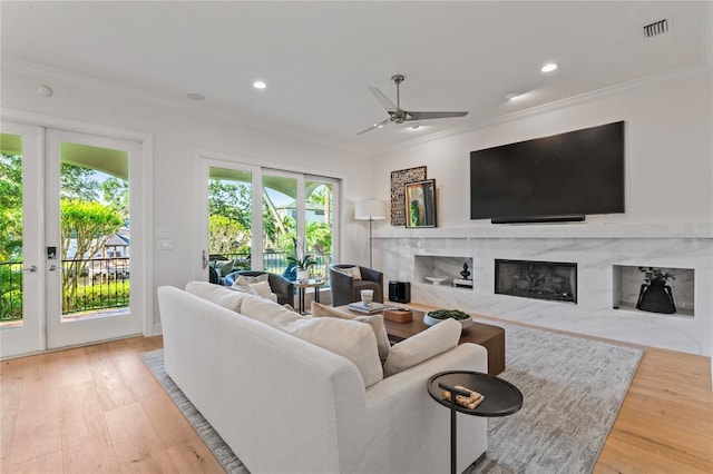 living room with ornamental molding, visible vents, ceiling fan, a high end fireplace, and wood finished floors