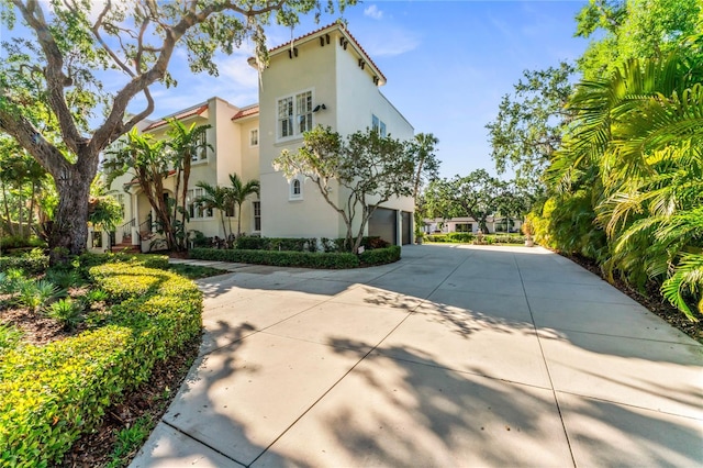 view of property exterior with an attached garage, driveway, stucco siding, and a tile roof