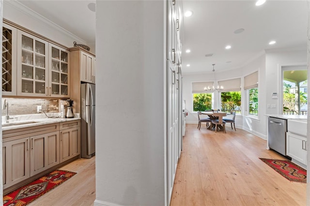 kitchen featuring tasteful backsplash, ornamental molding, appliances with stainless steel finishes, light wood finished floors, and a sink
