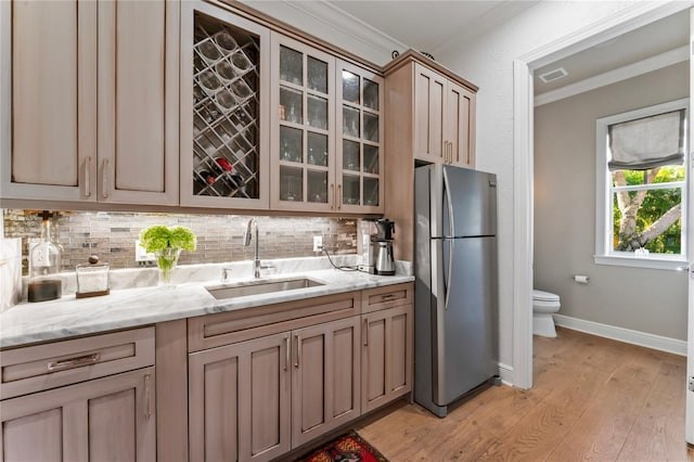 kitchen featuring ornamental molding, freestanding refrigerator, light wood-style floors, decorative backsplash, and a sink