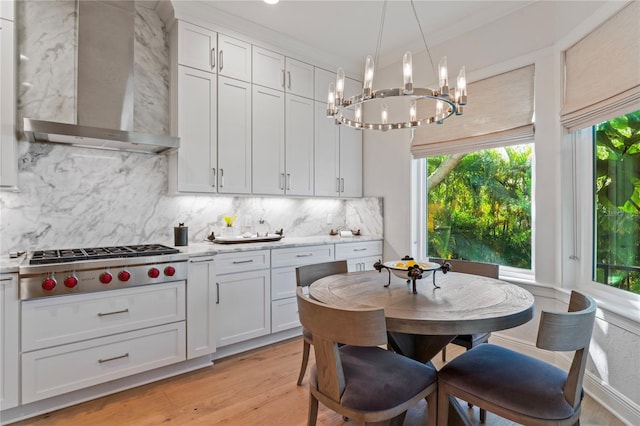 kitchen with tasteful backsplash, a chandelier, wall chimney exhaust hood, light wood finished floors, and stainless steel gas stovetop