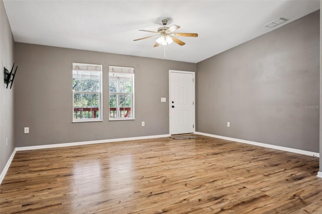 spare room with a ceiling fan, visible vents, wood finished floors, and baseboards