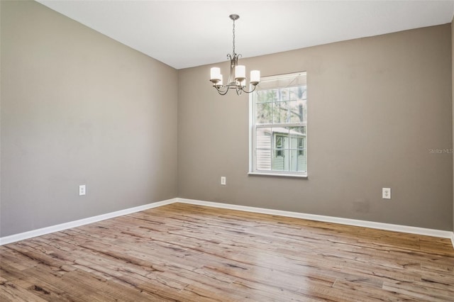 unfurnished room featuring a chandelier, baseboards, and wood finished floors