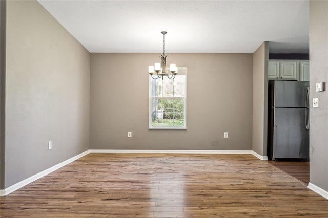 unfurnished dining area featuring a notable chandelier, baseboards, and wood finished floors