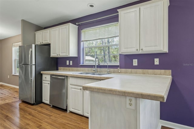 kitchen with a sink, appliances with stainless steel finishes, a peninsula, and white cabinetry