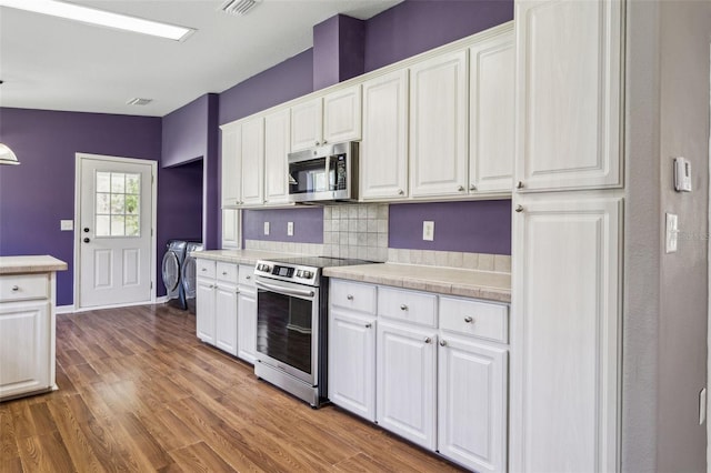 kitchen with light countertops, appliances with stainless steel finishes, white cabinets, wood finished floors, and washer and dryer