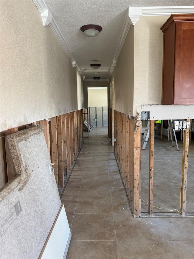 corridor featuring wooden walls, a textured wall, a wainscoted wall, a textured ceiling, and crown molding