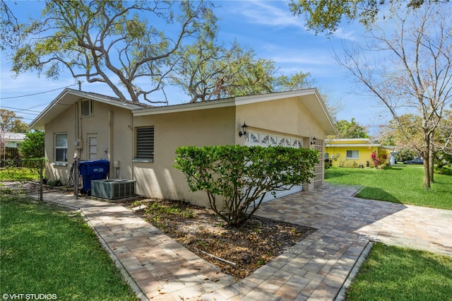 view of home's exterior featuring a garage, a yard, central AC unit, and stucco siding