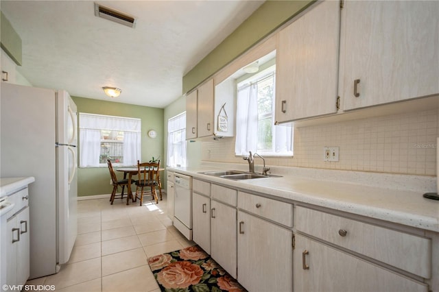 kitchen featuring light countertops, visible vents, backsplash, a sink, and white appliances