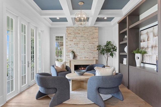 sitting room featuring a chandelier, a stone fireplace, coffered ceiling, wood finished floors, and beam ceiling