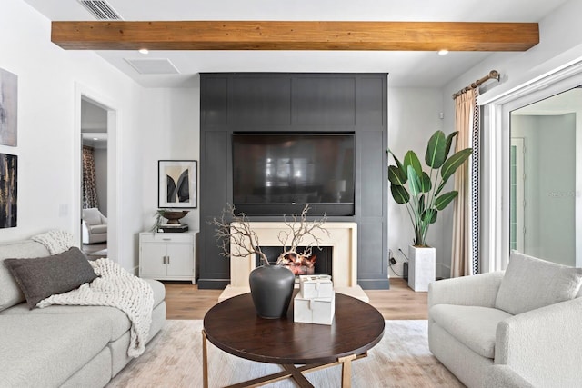 living room featuring beam ceiling, a high end fireplace, visible vents, and light wood-style floors