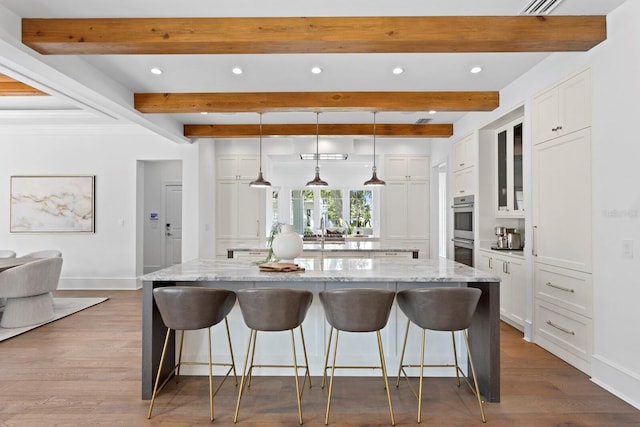 kitchen with double oven, a breakfast bar, white cabinetry, and a large island with sink