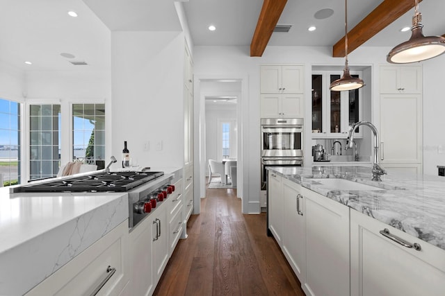 kitchen featuring appliances with stainless steel finishes, dark wood-type flooring, white cabinetry, a sink, and beamed ceiling