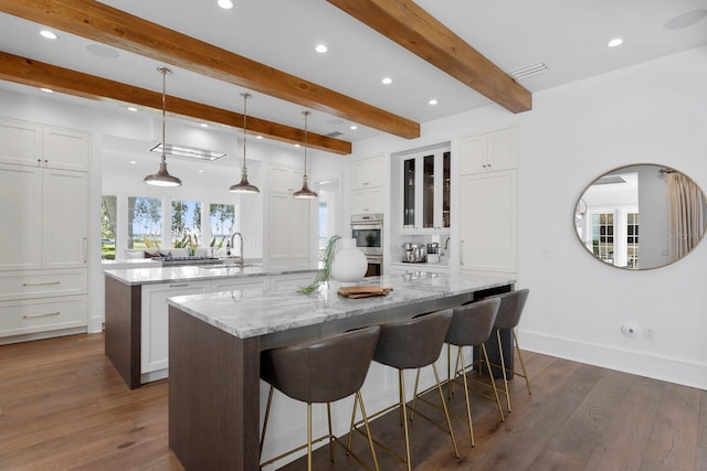 kitchen with a large island, a kitchen breakfast bar, dark wood-style flooring, white cabinetry, and a sink