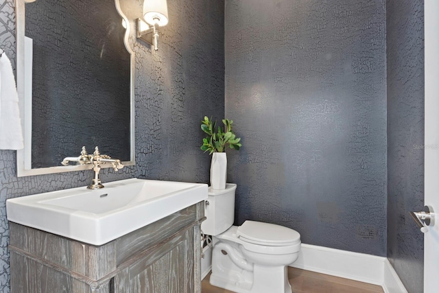 half bath featuring a textured wall, vanity, toilet, and baseboards