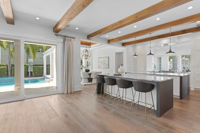 kitchen featuring a breakfast bar, a spacious island, wood finished floors, white cabinets, and light stone countertops