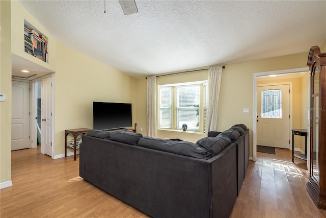 living room with lofted ceiling, a textured ceiling, light wood-type flooring, and baseboards