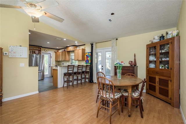 dining room with french doors, light wood finished floors, vaulted ceiling, a textured ceiling, and baseboards