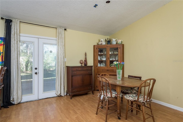 dining room featuring light wood-style floors, baseboards, a textured ceiling, and french doors