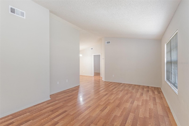 empty room with light wood-style floors, lofted ceiling, visible vents, and a textured ceiling