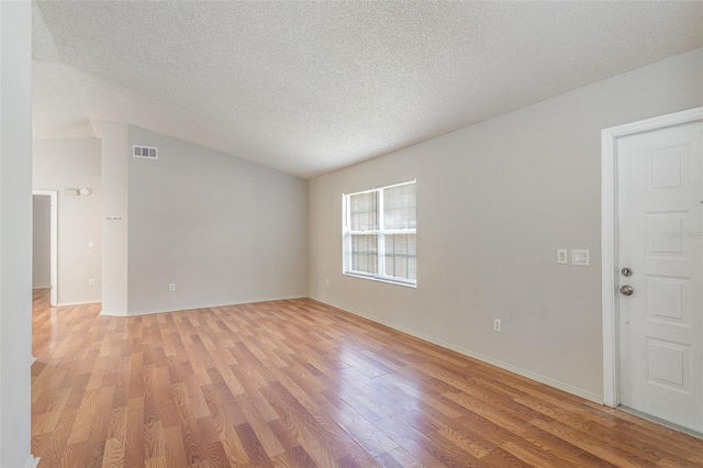 unfurnished room with a textured ceiling, visible vents, baseboards, vaulted ceiling, and light wood-style floors