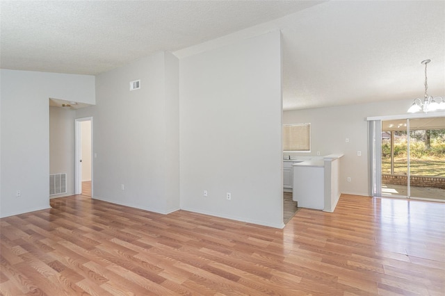 unfurnished living room with an inviting chandelier, a textured ceiling, visible vents, and light wood-style floors