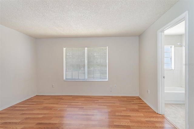 empty room with light wood-style floors, baseboards, and a textured ceiling