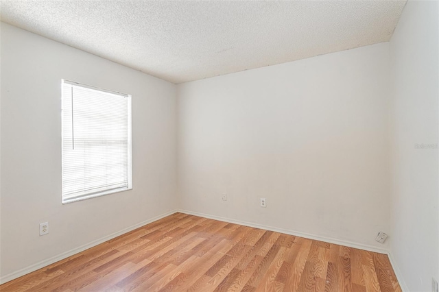 spare room with light wood-style floors, a textured ceiling, and baseboards