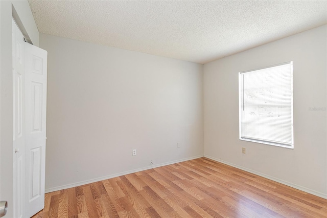 empty room featuring a textured ceiling, light wood-style flooring, and baseboards