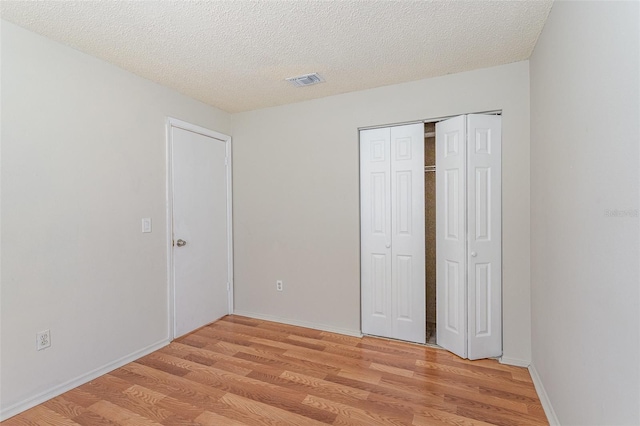 unfurnished bedroom with baseboards, visible vents, a textured ceiling, light wood-type flooring, and a closet