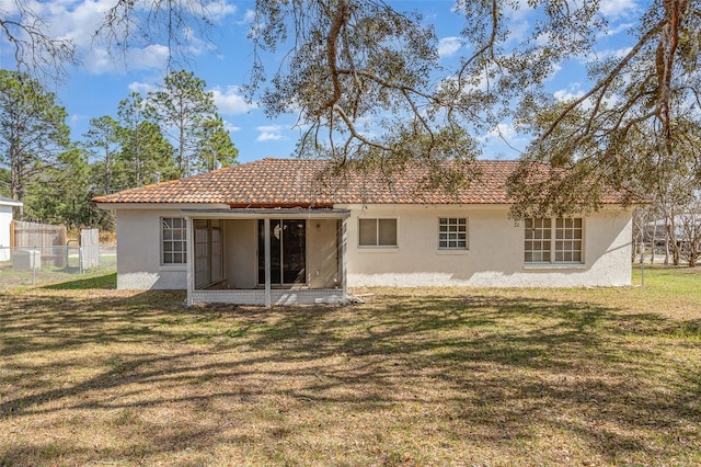 rear view of property featuring a yard, fence, a tiled roof, and stucco siding