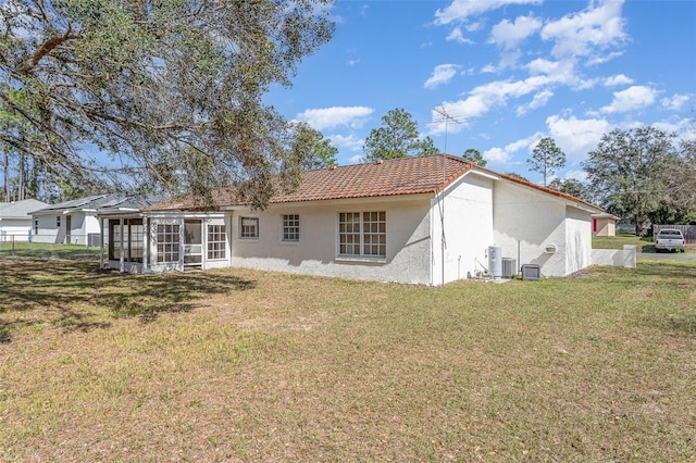 rear view of property with a yard, central AC, a sunroom, and stucco siding