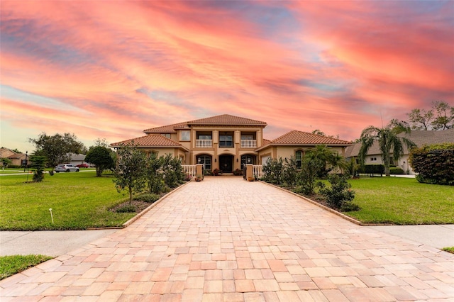 mediterranean / spanish-style house featuring a front yard, decorative driveway, a tile roof, and a balcony