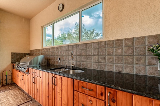 kitchen featuring brown cabinetry, dark stone counters, and a sink