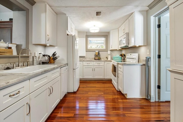 kitchen with dark wood-style floors, visible vents, white cabinets, a sink, and white appliances