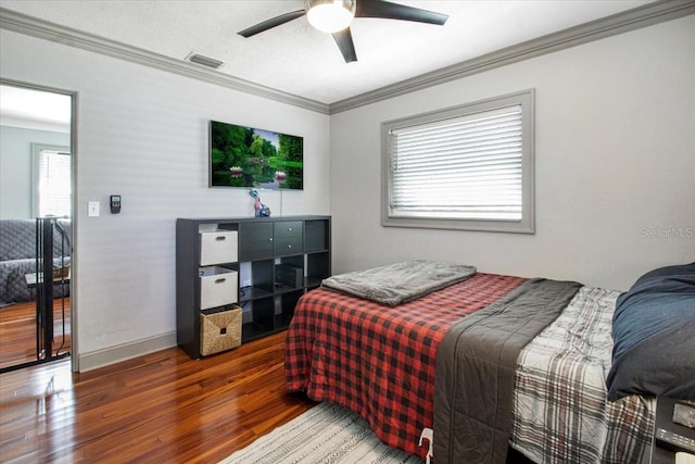 bedroom featuring visible vents, ornamental molding, a ceiling fan, wood finished floors, and baseboards