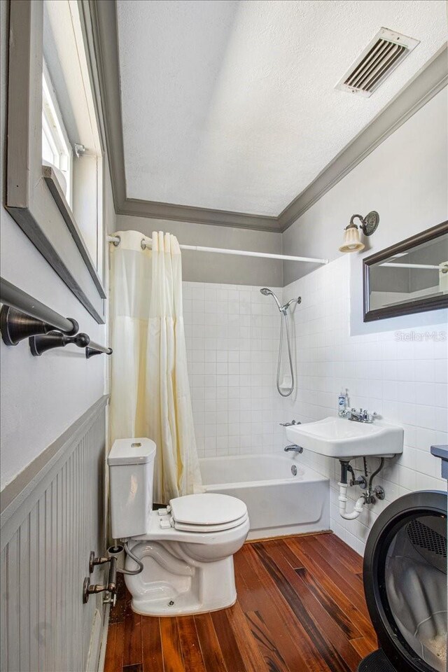 bathroom featuring a wainscoted wall, shower / tub combo with curtain, visible vents, toilet, and wood finished floors