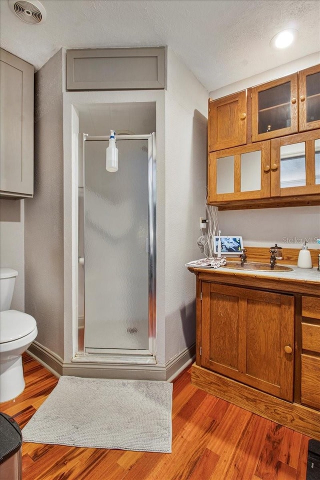 full bathroom featuring a stall shower, baseboards, visible vents, toilet, and wood finished floors