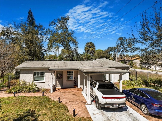 ranch-style house featuring driveway, fence, a carport, and stucco siding