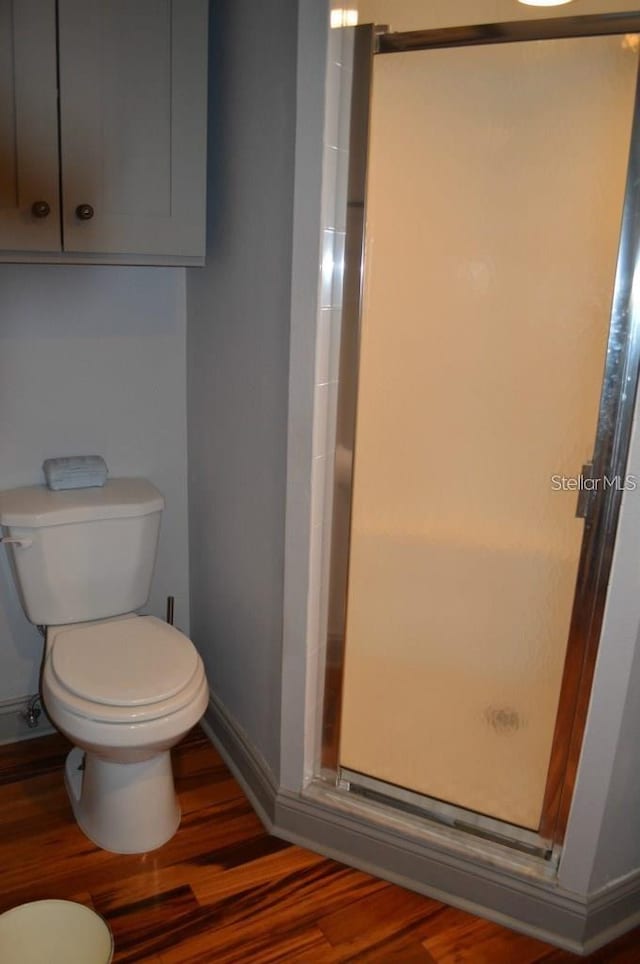 bathroom featuring wood finished floors, a shower stall, toilet, and baseboards