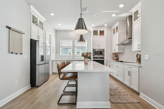 kitchen with visible vents, wall chimney exhaust hood, light countertops, appliances with stainless steel finishes, and backsplash