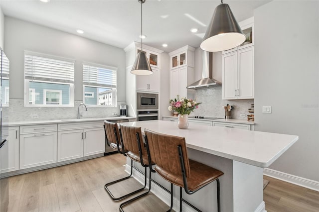kitchen featuring wall chimney exhaust hood, light countertops, appliances with stainless steel finishes, light wood finished floors, and a kitchen island