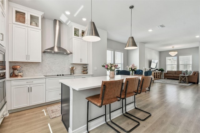 kitchen featuring black electric stovetop, wall chimney range hood, light countertops, a kitchen island, and visible vents