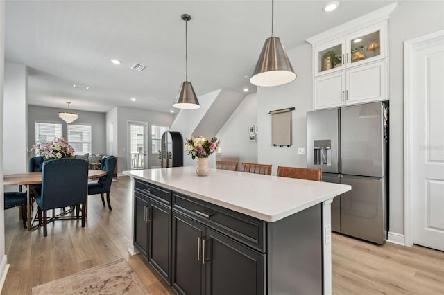 kitchen with stainless steel fridge with ice dispenser, light wood-style flooring, white cabinets, visible vents, and a kitchen island