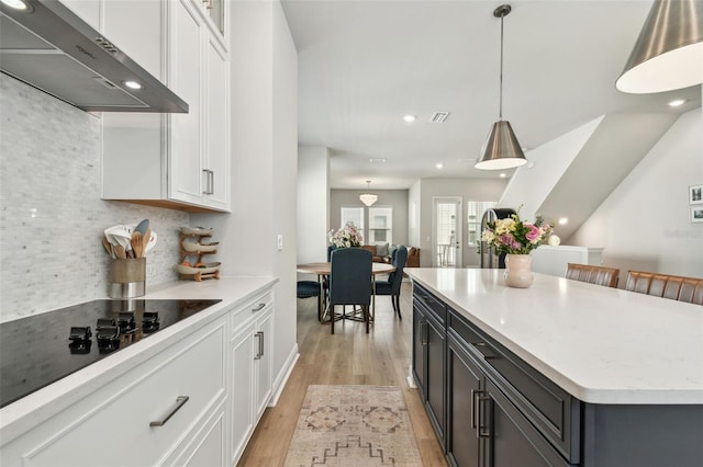 kitchen with light wood-style flooring, white cabinetry, wall chimney exhaust hood, black electric cooktop, and decorative backsplash