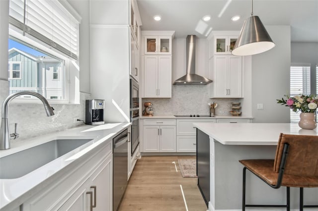 kitchen featuring a kitchen bar, wall chimney range hood, white cabinetry, a sink, and stainless steel appliances