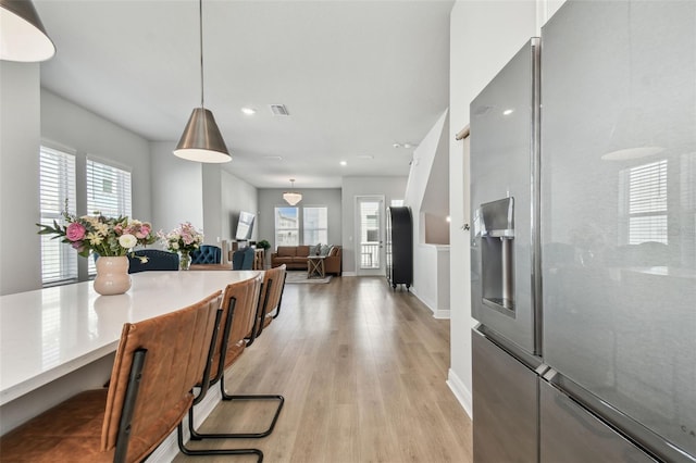 kitchen featuring light wood-style floors, pendant lighting, stainless steel fridge, and a wealth of natural light