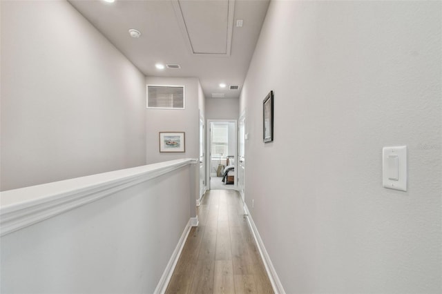 hall featuring visible vents, baseboards, attic access, and light wood-style floors
